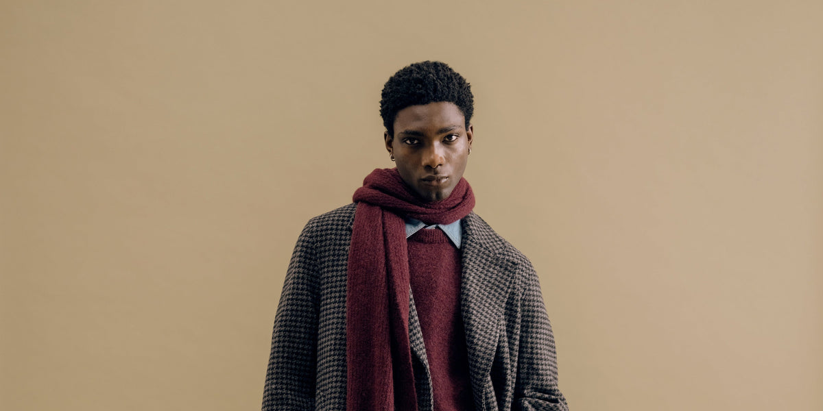A charcoal houndstooth overcoat with a burgundy scarf against a sand backdrop