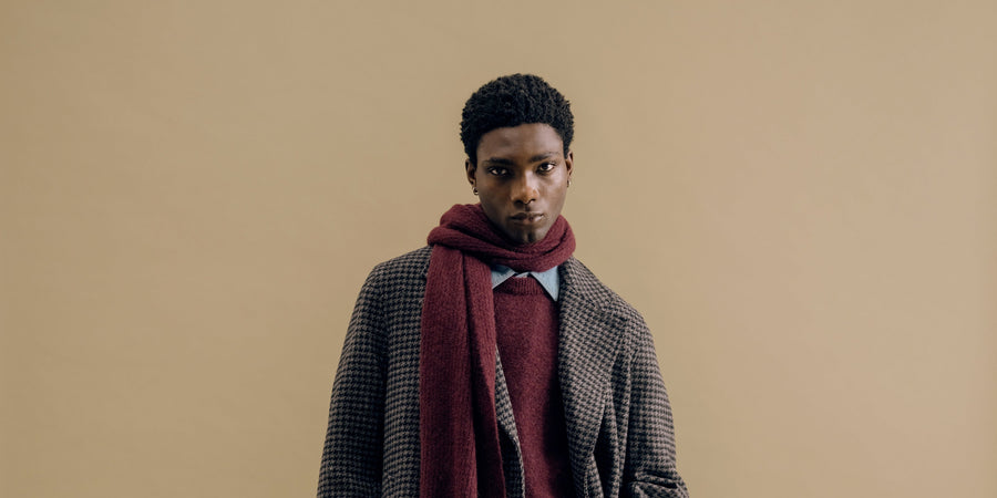 A charcoal houndstooth overcoat with a burgundy scarf against a sand backdrop