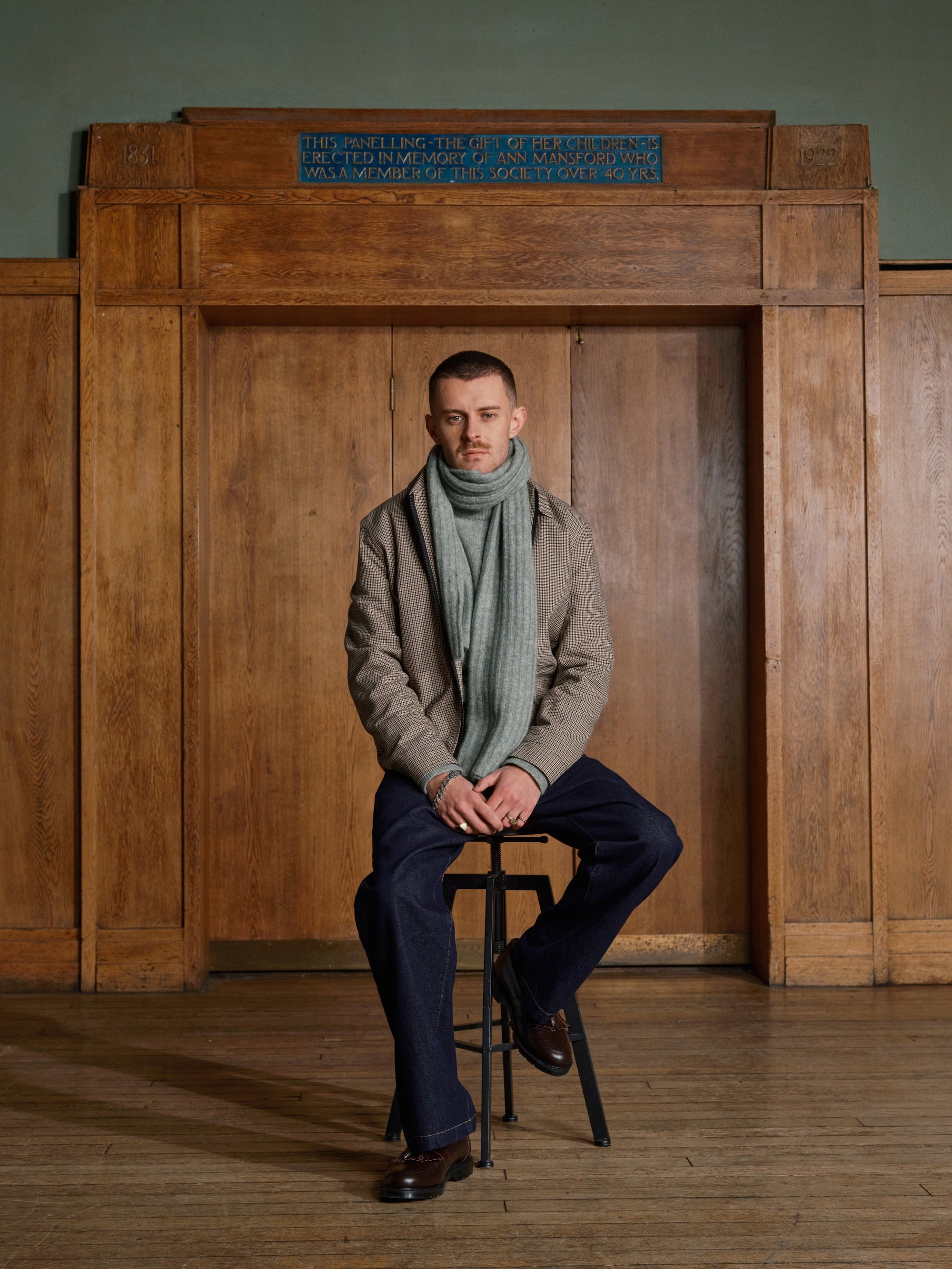 Model seated in a mint scarf and beige jacket