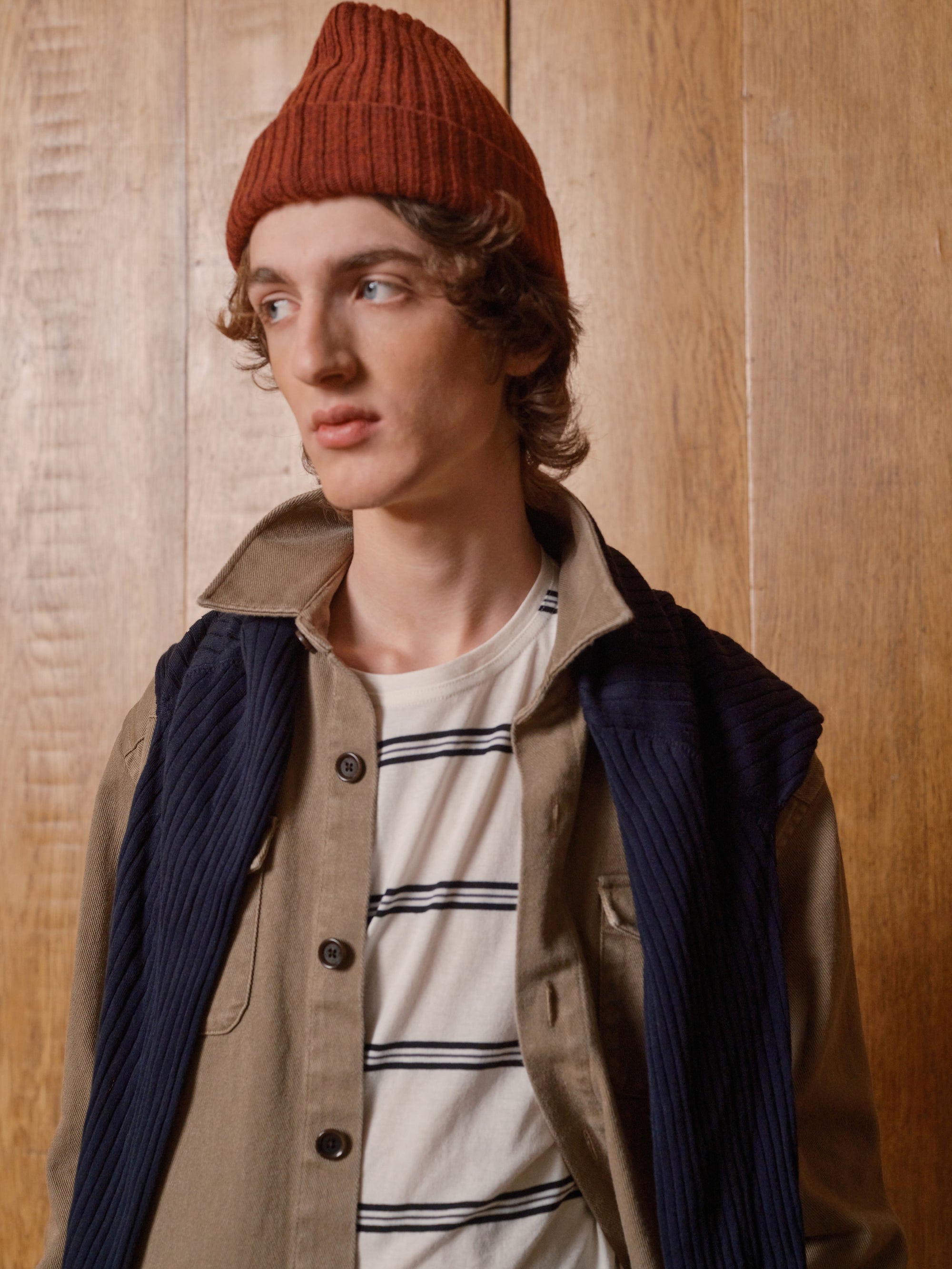 Model in a red beanie, striped tee and cord vest