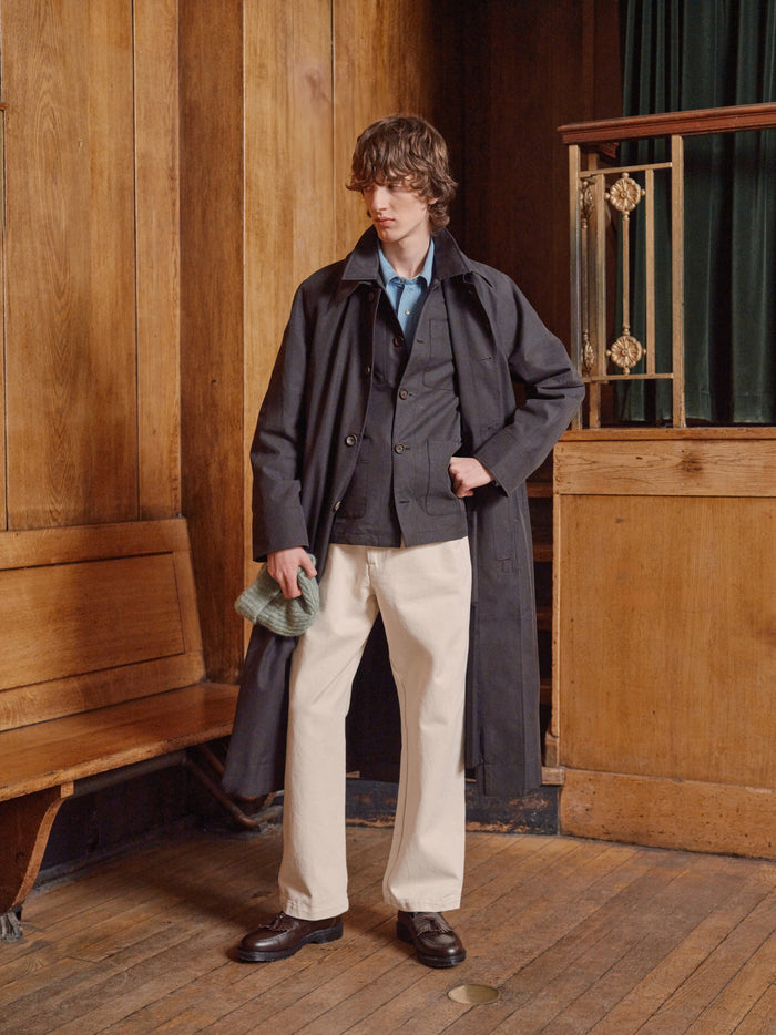 Model in ecru trousers with a pale blue shirt and grey coat