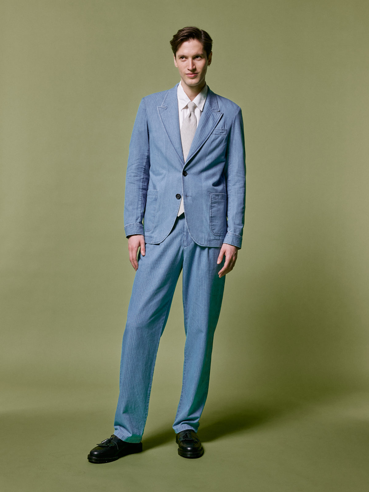 Pale blue double breasted suit with a white shirt and tie, against an olive backdrop.