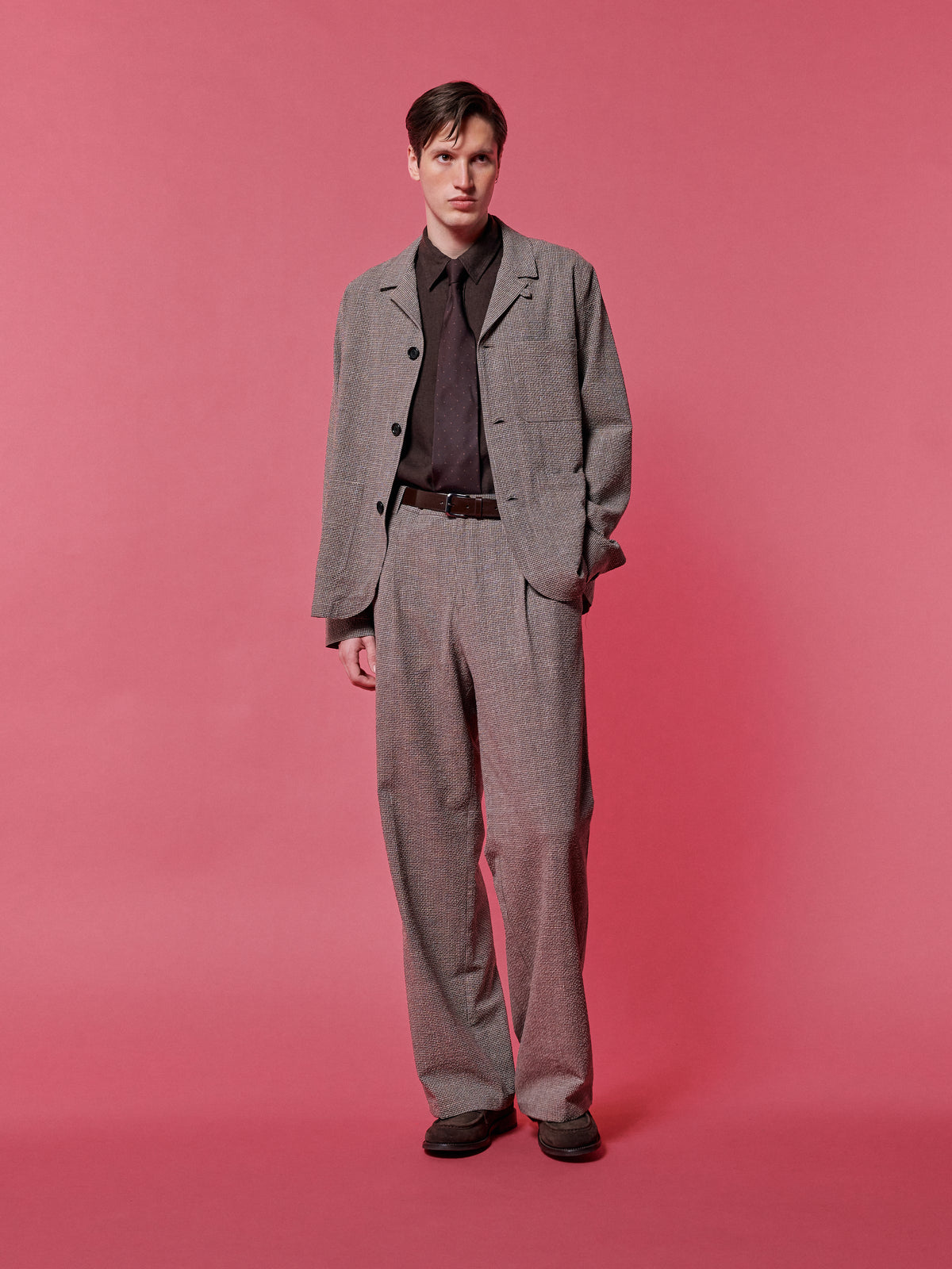 Grey check suit over a brown shirt, against a pink backdrop.