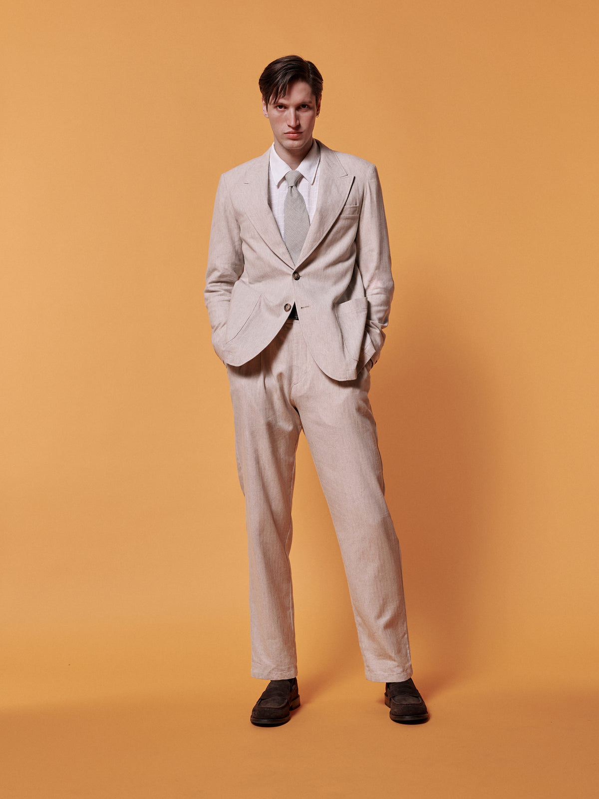 Cream suit with a white shirt and tie, against an ochre backdrop.