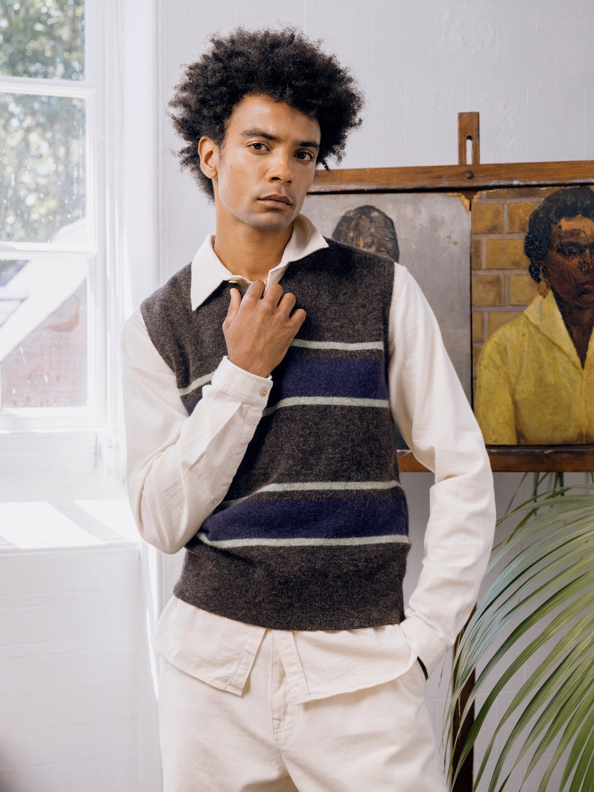 Brown and navy striped knitted vest over a cream shirt with ecru trousers.