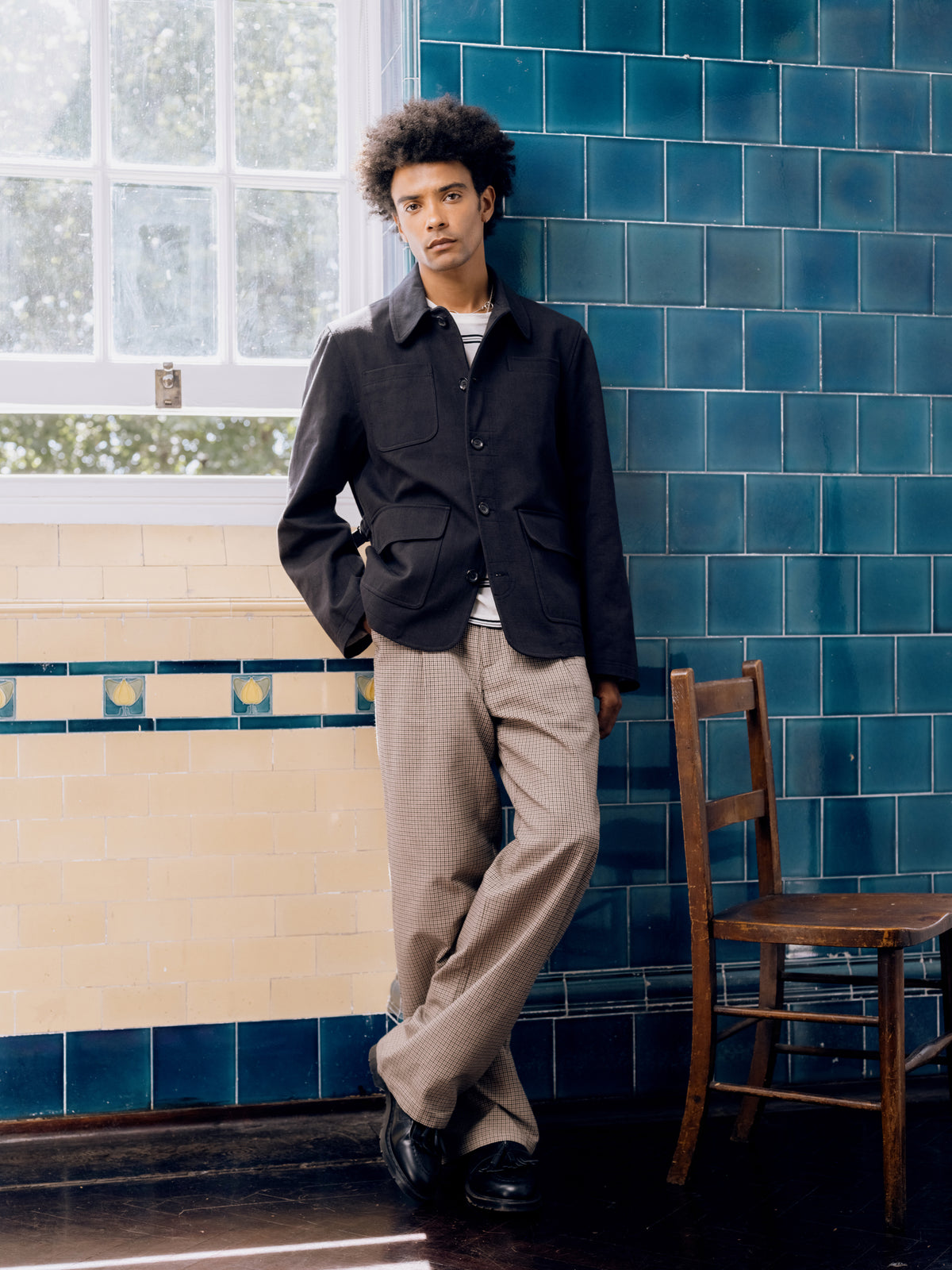Black Heath field jacket over a striped top with taupe trousers and black tassel loafers.