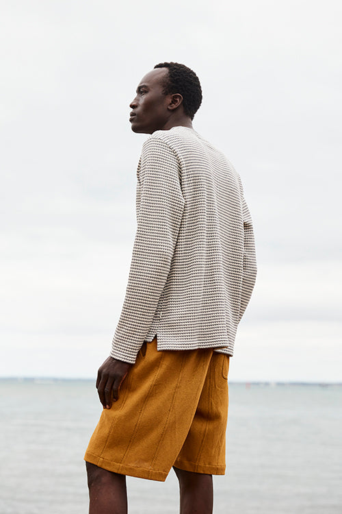 Oliver Spencer Spring 21, look 4. Rear view of an oatmeal jacket and tan shorts against a pale sky.