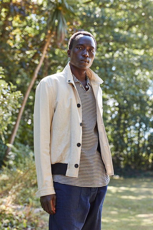 Oliver Spencer Spring 21, look 13. Oatmeal cardigan over a striped top with navy trousers.