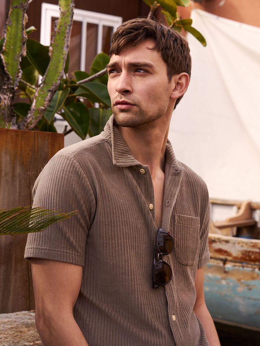 Oliver Spencer Summer 22 in Naples, look 1. Taupe short sleeve polo on a planted terrace above the street.