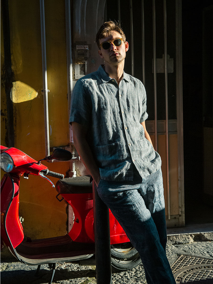 Oliver Spencer Summer 22 in Naples, look 3. Denim shirt and jeans with a red holdall in a doorway.