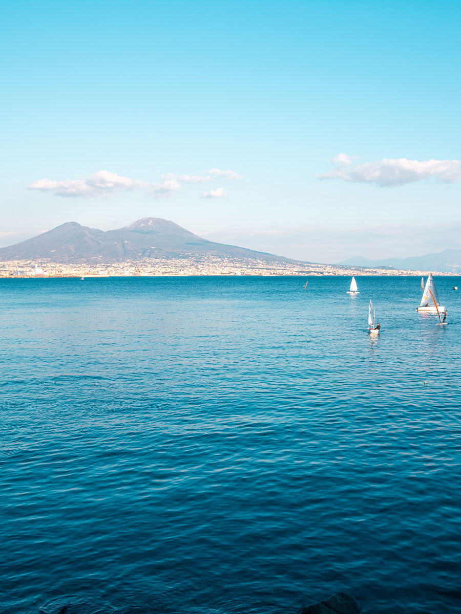 Oliver Spencer Summer 22 in Naples, look 8. The Bay of Naples with Vesuvius and sailing boats.