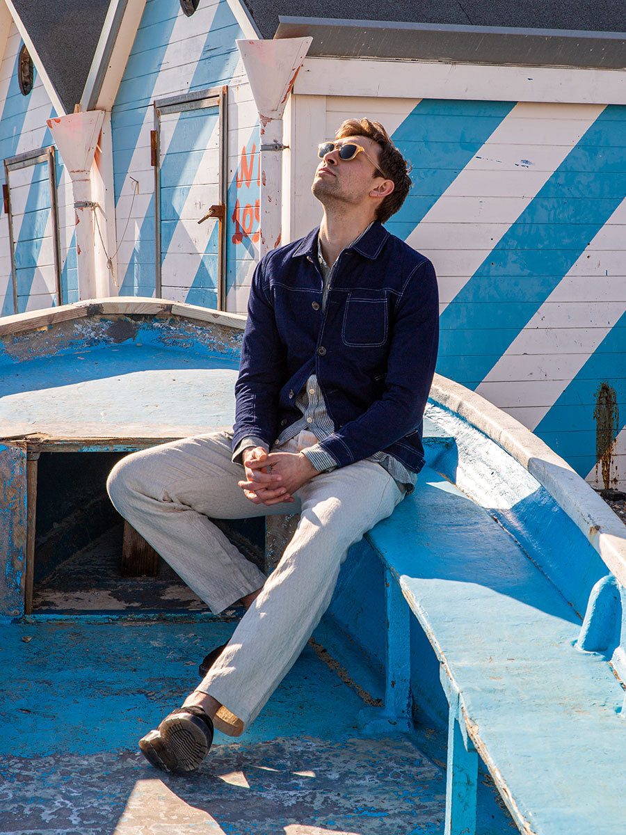 Oliver Spencer Summer 22 in Naples, look 9. Navy shirt, seated on a blue and white painted boat.