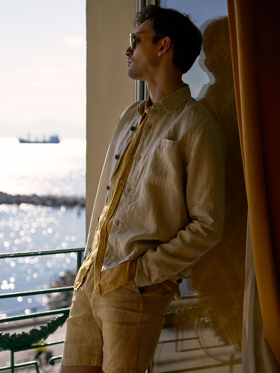 Oliver Spencer Summer 22 in Naples, look 10. Tan suit in a doorway, warm afternoon light.