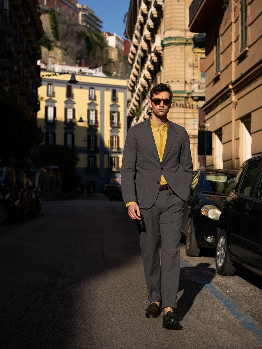 Oliver Spencer Summer 22 in Naples, look 13. Gold waistcoat and grey trousers in an arcade beside a scooter.