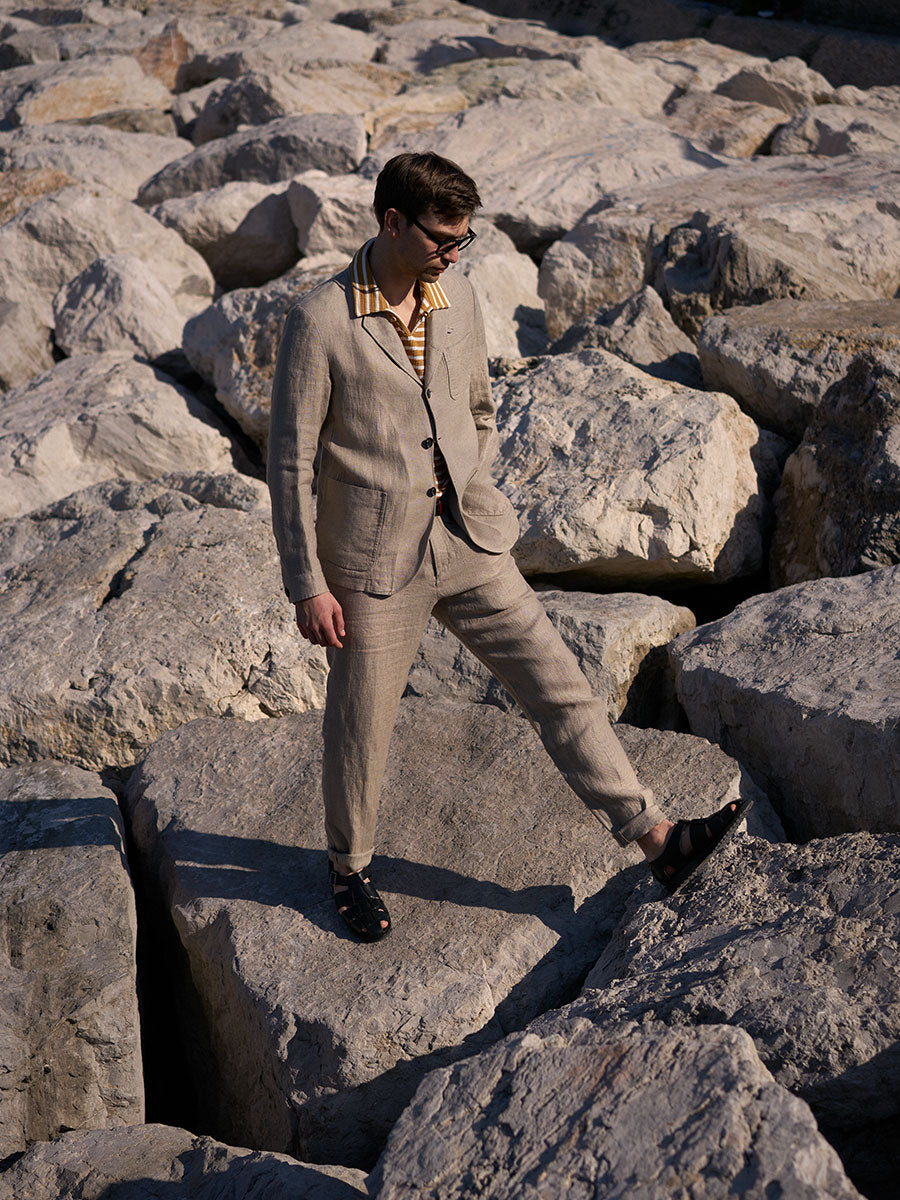 Oliver Spencer Summer 22 in Naples, look 14. Pale linen suit, reclining on volcanic rock.