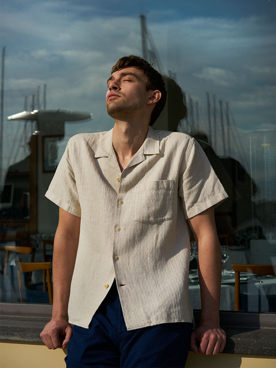 Oliver Spencer Summer 22 in Naples, look 20. Cream camp collar shirt against open sky.