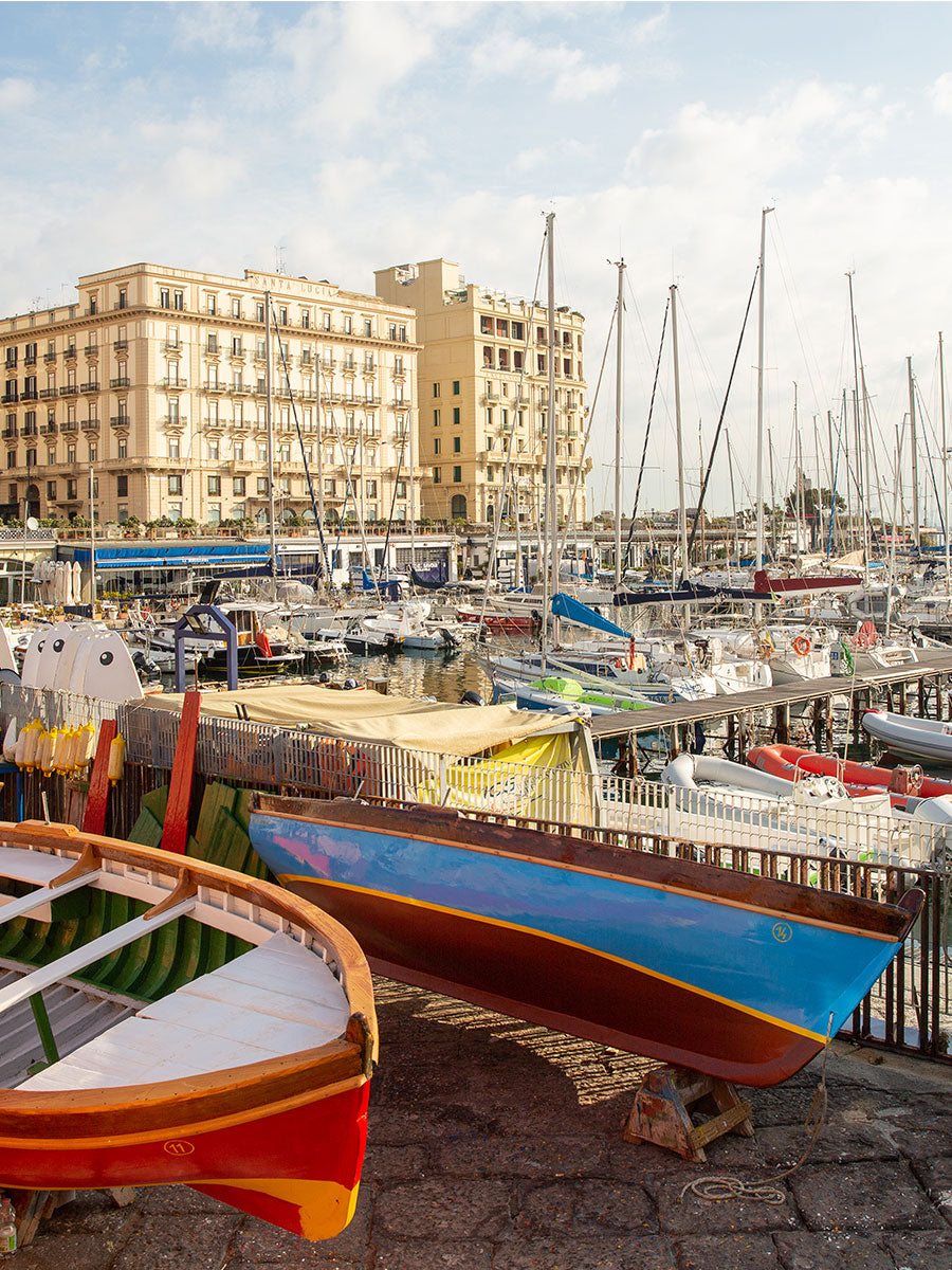 Oliver Spencer Summer 22 in Naples, look 21. The harbour at Mergellina, painted boats drawn up on the quay.