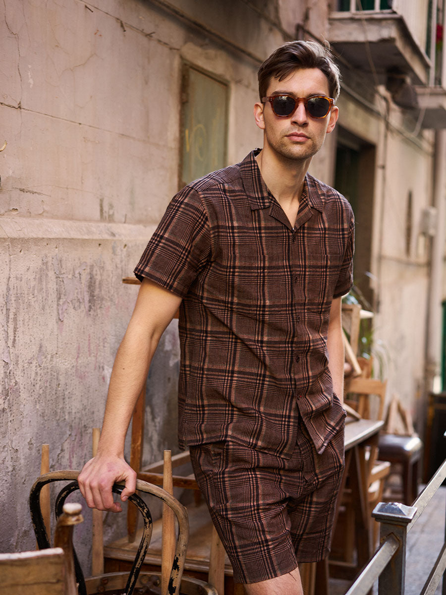 Oliver Spencer Summer 22 in Naples, look 25. Brown check short sleeve shirt and matching shorts in the street.